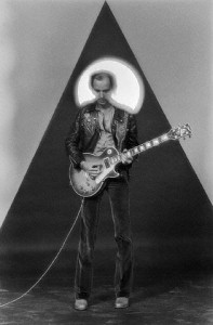 Peter Banks, guitarist for Yes, plays guitar against a backdrop of a triangle and a large circular light. Los Angleles. ca. 1970s Los Angeles, California, USA